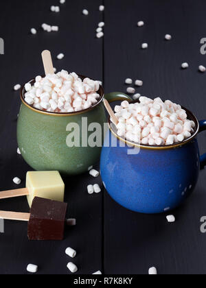 Deux tasses avec du chocolat chaud et des mini guimauves, une tasse d'être bleu et l'autre vert, avec des cubes de chocolat blanc et noir, brun foncé sur le dos Banque D'Images
