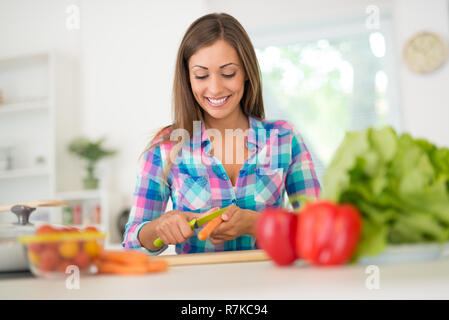 Belle jeune femme faisant des repas dans la cuisine domestique. Elle s'écaille sur la carotte cuisine conseil. Banque D'Images