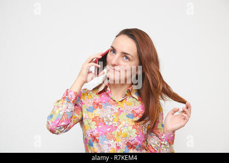 Portrait d'une belle jeune fille dans une chemise colorée à parler au téléphone à jouer avec les cheveux. sur un fond blanc. brown couleur de cheveux. Banque D'Images