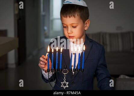 Garçon juif caucasien mignon bougies d'éclairage sur un traditionnel Hanukkah menorah candélabre, fêtes juives concept. Banque D'Images