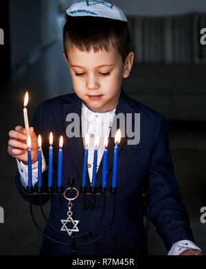 Garçon juif caucasien mignon bougies d'éclairage sur un traditionnel Hanukkah menorah candélabre, fêtes juives concept. Banque D'Images