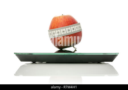Enveloppé d'Apple avec un ruban à mesurer sur une balance de cuisine numérique. Plus isolé sur fond blanc.Concept de régimes et d'une saine alimentation. Banque D'Images