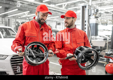 Portrait de deux mécaniciens auto en uniforme rouge debout avec des disques pour l'alignement des roues sur la voiture publique Banque D'Images