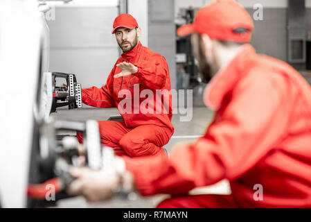Deux mécaniciens auto en uniforme rouge disque de fixation de roue pour l'alignement sur une voiture de luxe au service de voiture Banque D'Images