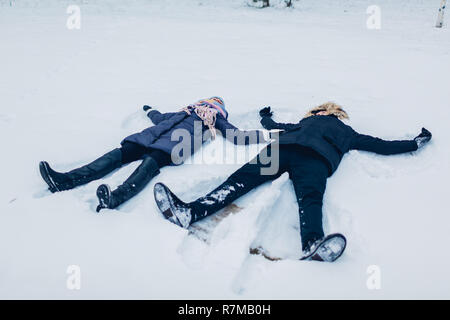 Beau couple aimant faire des anges dans la neige en hiver forêt couchée dans la neige. Les gens heureux s'amuser en plein air Banque D'Images