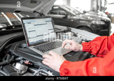 Mécanicien auto diagnostic moteur de voiture avec un ordinateur portable avec un programme spécial, close-up view avec pas de visage Banque D'Images