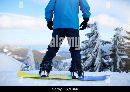 Vue arrière de snowboarder jambes sur son arrière-pays avant session freeride dans la forêt. Les pieds de l'homme in Boots snowboard moderne monté dans un débit rapide fixe liaisons avec des courroies. Rider at ski resort. Banque D'Images