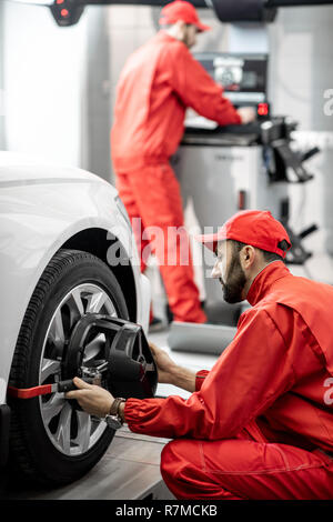 Mécanicien auto beau en uniforme rouge pour disque de fixation à l'alignement des roues de voiture Banque D'Images