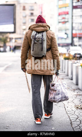 Une vue arrière du sans-abri mendiant la marche à l'extérieur de l'homme dans la ville, tenant un sac. Banque D'Images