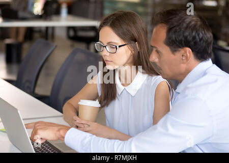 Mentor d'âge moyen avec le travail à l'ordinateur aide intern Banque D'Images