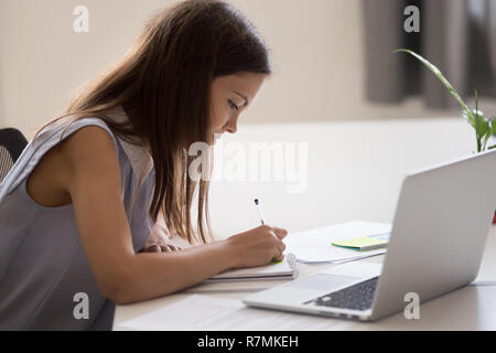 Young Girl holding pen, en prenant des notes, en travaillant avec un ordinateur portable Banque D'Images