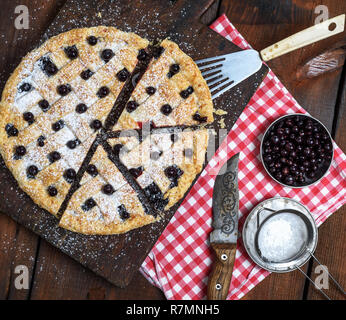 Cassis ronde au four gâteau coupé en morceaux et saupoudré de sucre en poudre sur une planche en bois brun Banque D'Images