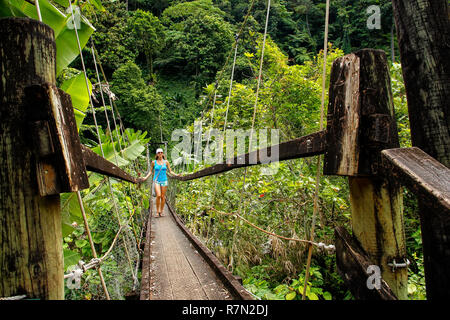 Jeune femme marche sur pont suspendu au-dessus de Wainibau stream, Lavena promenade côtière, l'île de Taveuni (Fidji). Taveuni est la troisième plus grande île des Fidji. Banque D'Images