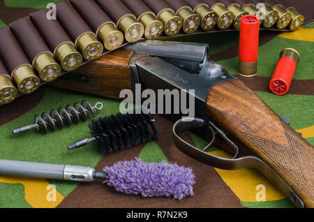 Fusil de chasse et des munitions avec des brosses pour le nettoyage des armes nucléaires se trouvant sur un fond de camouflage. Banque D'Images