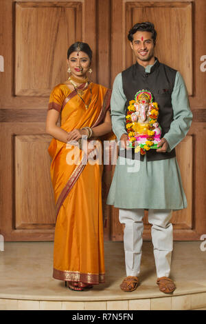 Portrait of happy couple maharashtrian en vêtements traditionnels célébrant festival ganapati tenant une petite statue de seigneur ganesha. Banque D'Images