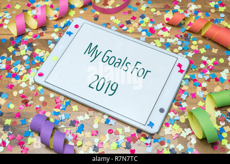Confettis et Serpentins de papier coloré sur table en bois en arrière-plan avec tablette blanche et mes objectifs pour 2019 message écrit sur l'écran Banque D'Images