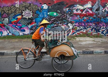 L'Indonésie, de Java, Yogyakarta, location rickshaw devant un mur décoré de graffitis Banque D'Images