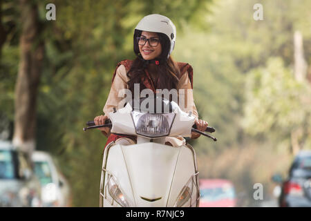 Jeune femme portant des lunettes et un casque riding scooter à la route. Banque D'Images