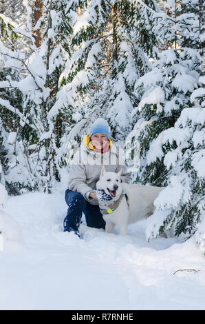 Femme joyeuse avec un chien blanc dans la forêt couverte de neige d'hiver Banque D'Images