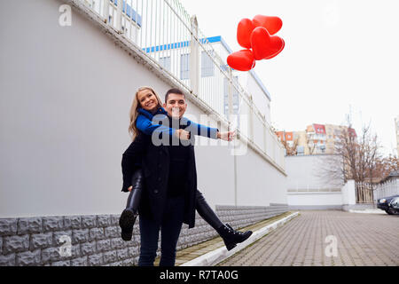 Fille sur le dos de gars avec des ballons coeur rouge dans la rue. Banque D'Images