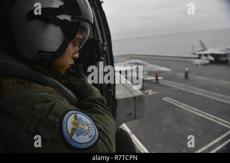 Océan Pacifique (3 avril 2017) Naval Air Crewman (hélicoptère) 3e classe Jason Cardena, originaire de Houston, est assis à la porte d'un MH-60R Sea Hawk, à partir de la 'Wolf Pack' d'Hélicoptère grève Maritime Squadron (HSM) 75, qu'il atterrit sur le porte-avions USS Nimitz (CVN 68), tout en participant à une démonstration de force de l'exercice en commun du détroit. Nimitz est actuellement en cours d'exercice de l'unité de formation Composite (COMPTUEX) avec le groupe aéronaval du Nimitz en préparation pour un prochain déploiement. COMPTUEX teste un groupe aéronaval a pour mission de préparation et de capacité à fonctionner comme un Banque D'Images