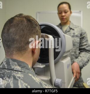 Le sergent de l'US Air Force. Carson River, 8e Escadron d'opérations médicales technicien en santé publique s'applique, son front à l'auto réfractomètre en tant que Senior Airman Kiara Warren, 51e Escadron en médecine aérospatiale technicien d'optométrie, emploie la machine à Kunsan Air Base, République de Corée, le 24 mars 2017. Le réfractomètre automatique mesure la courbure de l'œil et permet une numérisation pour donner une base de prescription pour les yeux. Banque D'Images