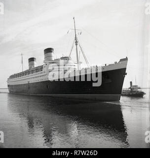 Années 1950, historique, le RMS Queen Elizabeth mis à quai par un remorqueur. Le steamship est un paquebot qui a fourni un service de ligne de luxe bewtween Southampton et New York aux Etats-Unis, via Cherbourg en France. Construit par John Brown & Co à Clydebank, en Écosse, lors de son lancement en 1938, il était le plus grand paquebot jamais construit et le sont restés pendant 56 ans par la suite. Elle était utilisée comme dans WW2, à bord. Banque D'Images