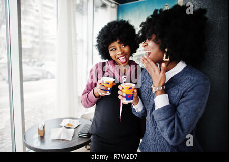 Deux cheveux bouclés african american woman l'usure sur les chandails avec des tasses de thé posée au café à l'intérieur. Banque D'Images