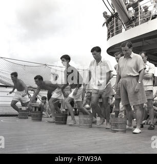 Années 1950, historique, mi-océan et passagers de sexe masculin à l'extérieur, sur le pont d'un château-union steamship jouant un jeu de carte comportant l'exécution et de fûts en bois. Banque D'Images