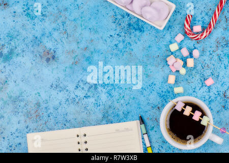 Tasse à café et les guimauves, vierge ouvrir bloc-notes avec stylo sur résumé fond bleu. Vue d'en haut. Télévision immersive. espace pour texte. Banque D'Images