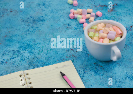 Tasse à café et les guimauves, vierge ouvrir bloc-notes avec stylo sur résumé fond bleu. Vue d'en haut. Télévision immersive. espace pour texte. Banque D'Images