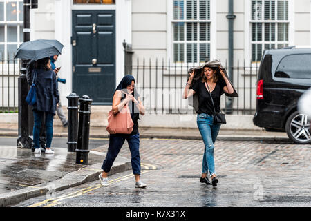 Londres, Royaume-Uni - 12 septembre 2018 : les gens, femmes, femmes couvrant la tête avec des vêtements, pulls, veste randonnée avec parasols dans rainy météorologiques sur sid Banque D'Images