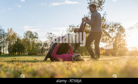 Jeune famille de quatre playing in autumn park lying in grass mère avec son petit garçon de levage et père de tourner autour de l'autre fils tenant son ha Banque D'Images