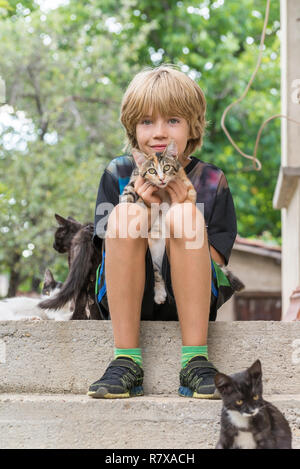 Adorable garçon tenant un chaton, assis sur des escaliers Banque D'Images