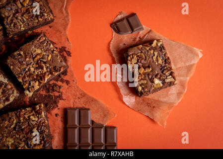 Brownie aux noix gâteau coupé en morceaux et les côtelettes de chocolat sur du papier sulfurisé. Vue directement au-dessus avec un fond de couleur orange Banque D'Images