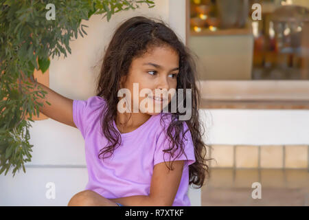 Belle petite fille tient à une succursale tout en s'appuyant sur un mur à la route. Portant une chemise de couleur solide violet clair avec des cheveux en désordre shabby chic. Banque D'Images