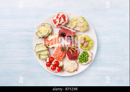 De savoureux canapés de saumon fumé, concombre, cerisier, de la mozzarella, les oeufs, les champignons, les olives, l'avocat, les amandes servi sur une assiette. Banque D'Images