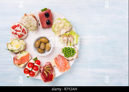 Canape savoureux avec du saumon fumé, concombre, oeufs, mozzarella, champignons, olives, avocat, amande servi sur une assiette. Banque D'Images