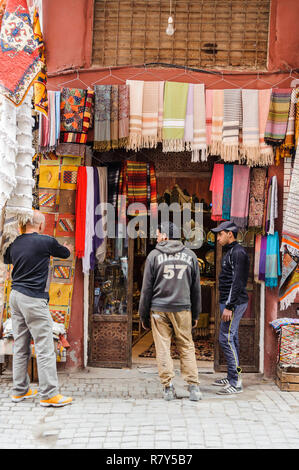 05-03-15, Marrakech, Maroc. Scène de rue dans le souk, dans la médina. Les jeunes hommes se tiennent à l'extérieur d'un magasin qui vend des tissus de couleurs vives. Photo : © Carte SIM Banque D'Images