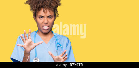 Young african american woman médecin isolé plus de peur d'arrière-plan et terrifié par la peur d'arrêt expression geste avec les mains, criant sous le choc. Pan Banque D'Images