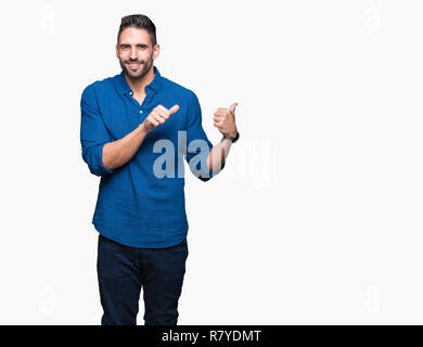 Jeune homme séduisant sur fond isolé en pointant sur l'arrière derrière avec la main et Thumbs up, souriant confiant Banque D'Images