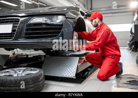 Mécanicien Auto en uniforme rouge voiture de sport entretien Contrôle de freins avant dans le service de voiture Banque D'Images