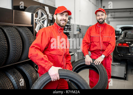 Portrait d'un service de location de deux travailleurs en uniforme rouge se tenant ensemble avec de nouveaux pneus au magasin Banque D'Images