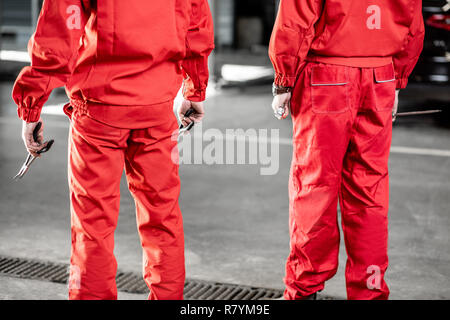 Deux mécaniciens auto en uniforme rouge debout ensemble dans la voiture, vue arrière Banque D'Images