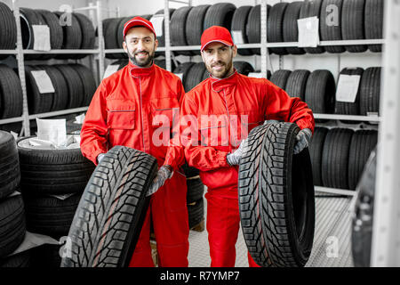 Portrait de deux travailleurs en uniforme rouge avec des pneus de voiture à l'entrepôt du service de voiture Banque D'Images