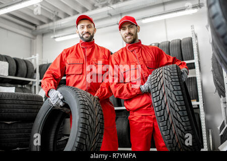 Portrait de deux travailleurs en uniforme rouge avec des pneus de voiture à l'entrepôt du service de voiture Banque D'Images