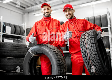 Portrait de deux travailleurs en uniforme rouge avec des pneus de voiture à l'entrepôt du service de voiture Banque D'Images