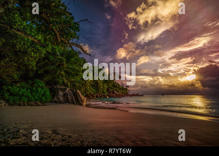 Coucher du soleil sur la plage pittoresque de rêve à anse georgette sur Praslin sur les seychelles. Un gros rocher de granit, l'eau turquoise, des palmiers et un ciel romantique.. Banque D'Images