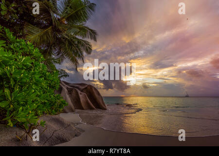 Coucher du soleil sur la plage pittoresque de rêve à anse georgette sur Praslin sur les seychelles. Un gros rocher de granit, l'eau turquoise, des palmiers et un ciel romantique.. Banque D'Images