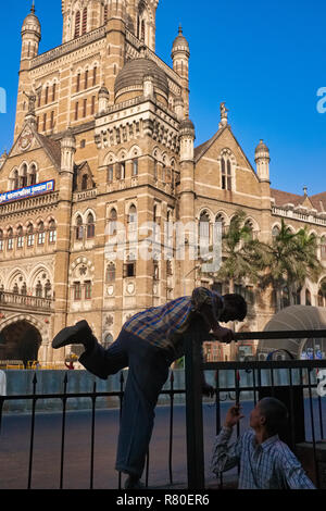 Un homme en face de la Corporation municipale de l'ère coloniale Building à Mumbai, Inde, grimpe sur une clôture pour éviter un détour Banque D'Images